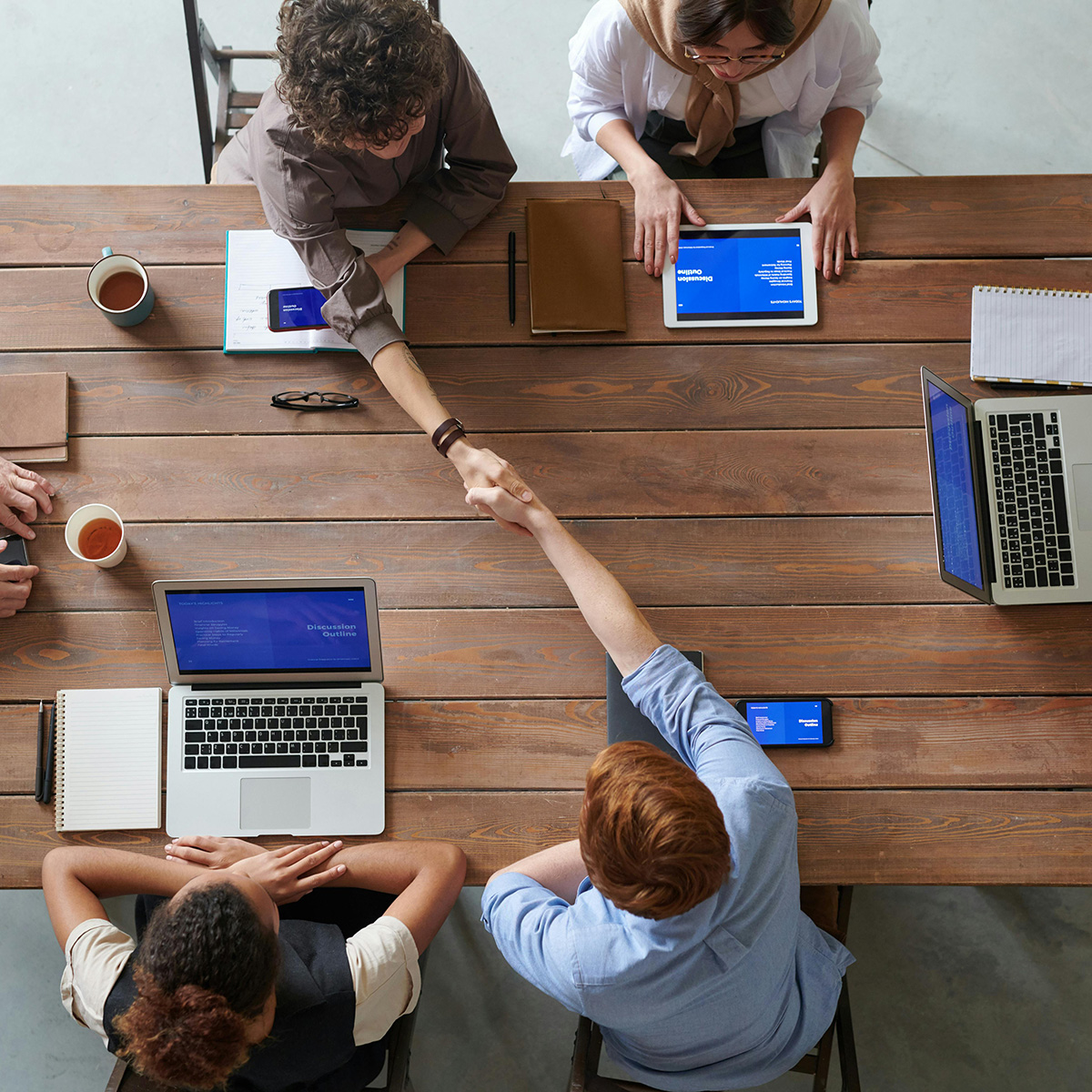 People at a table on their devices shaking hands. 